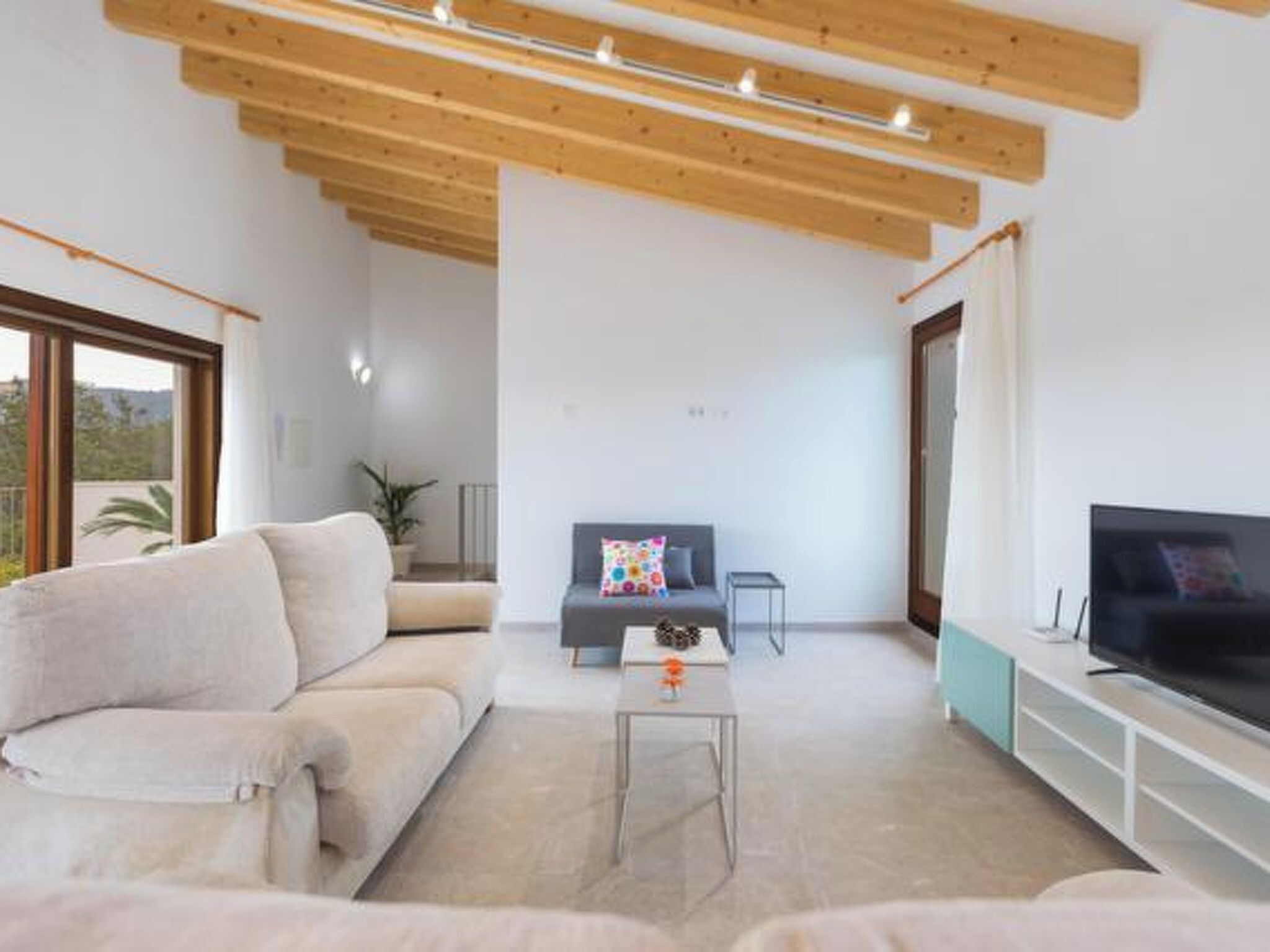Een moderne woonkamer met een bank, een salontafel, een televisie en een houten plafondconstructie.