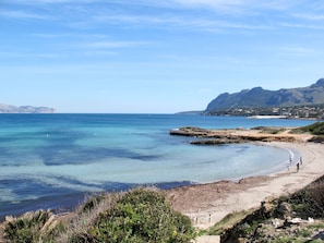 Ein Küstenstrand mit klarem Wasser, Felsenformationen und einer entfernten Bergkette.