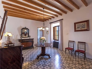 A room with a checkered floor, wooden beams on the ceiling, a round table with a vase, two chairs, a dresser, and a mirror. - Caballeria 16 Familiar by Interhome (Bunyola)