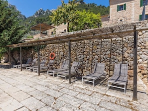 A stone wall with a wooden pergola and lounge chairs. - Caballeria 16 Familiar by Interhome (Bunyola)