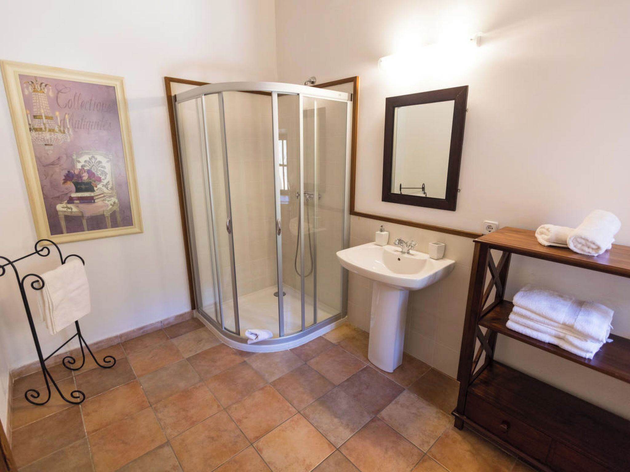 Un bany amb dutxa de vidre, un lavabo, un mirall i un suport per a tovalloles.