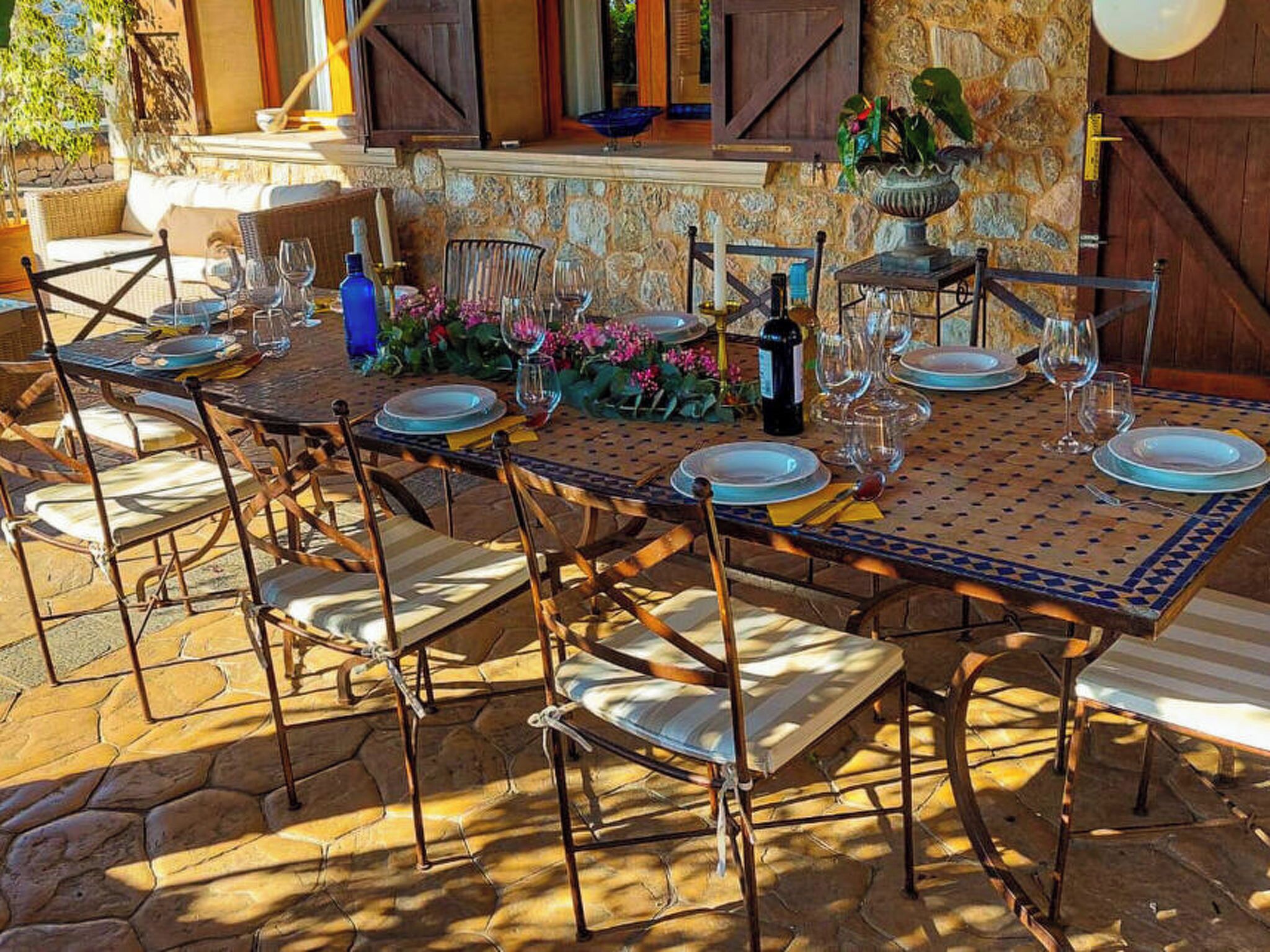 An outdoor dining area with a stone wall, a table set for six, and chairs with cushioned seats.