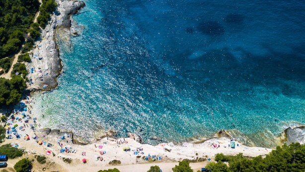 An aerial view of a beach with clear turquoise waters, rocky coastline, and numerous beach umbrellas and sun loungers. - Villa Markulin by Interhome (Bokordici)