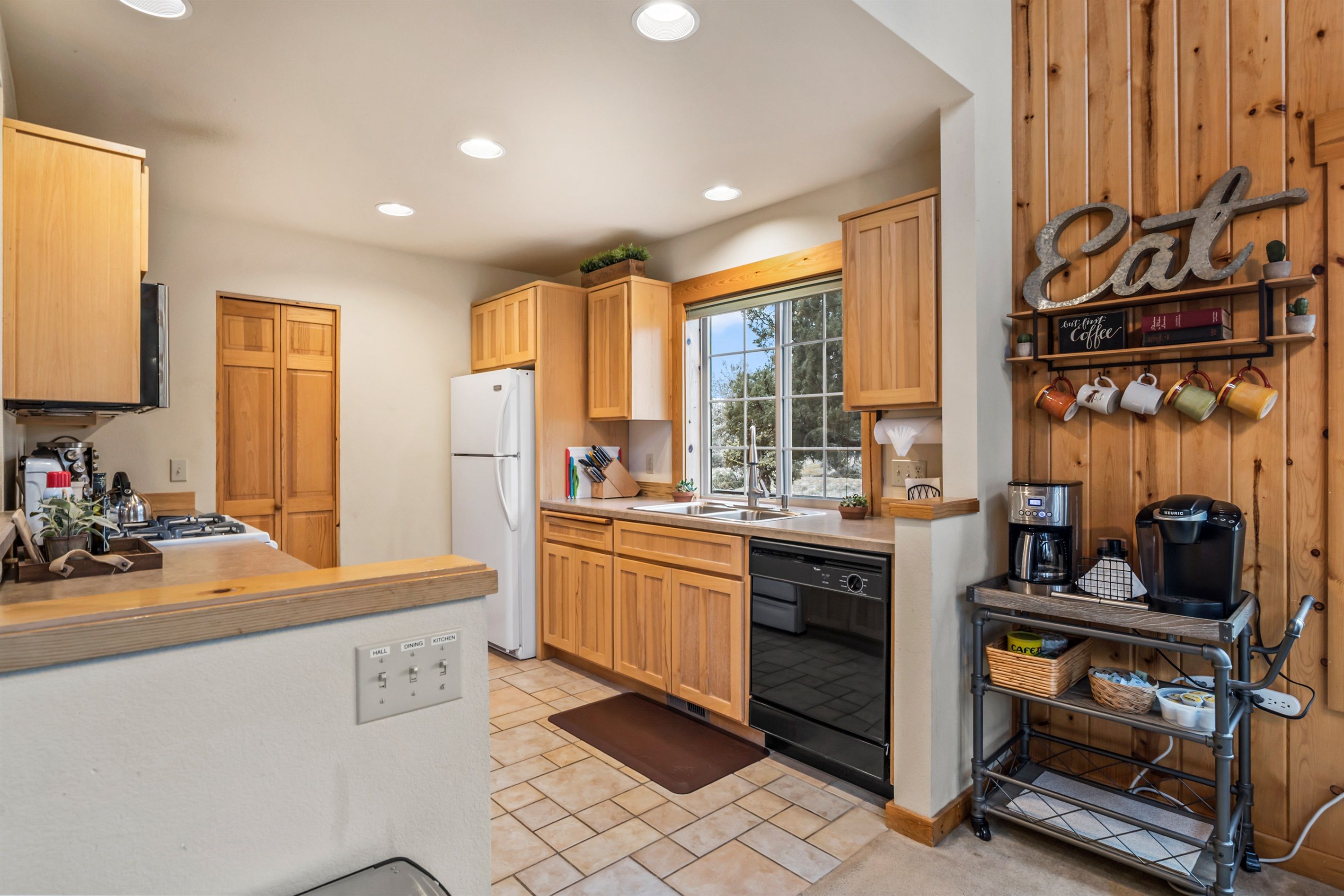 A kitchen with wooden cabinets, a dishwasher, a coffee station, and a window with a view.