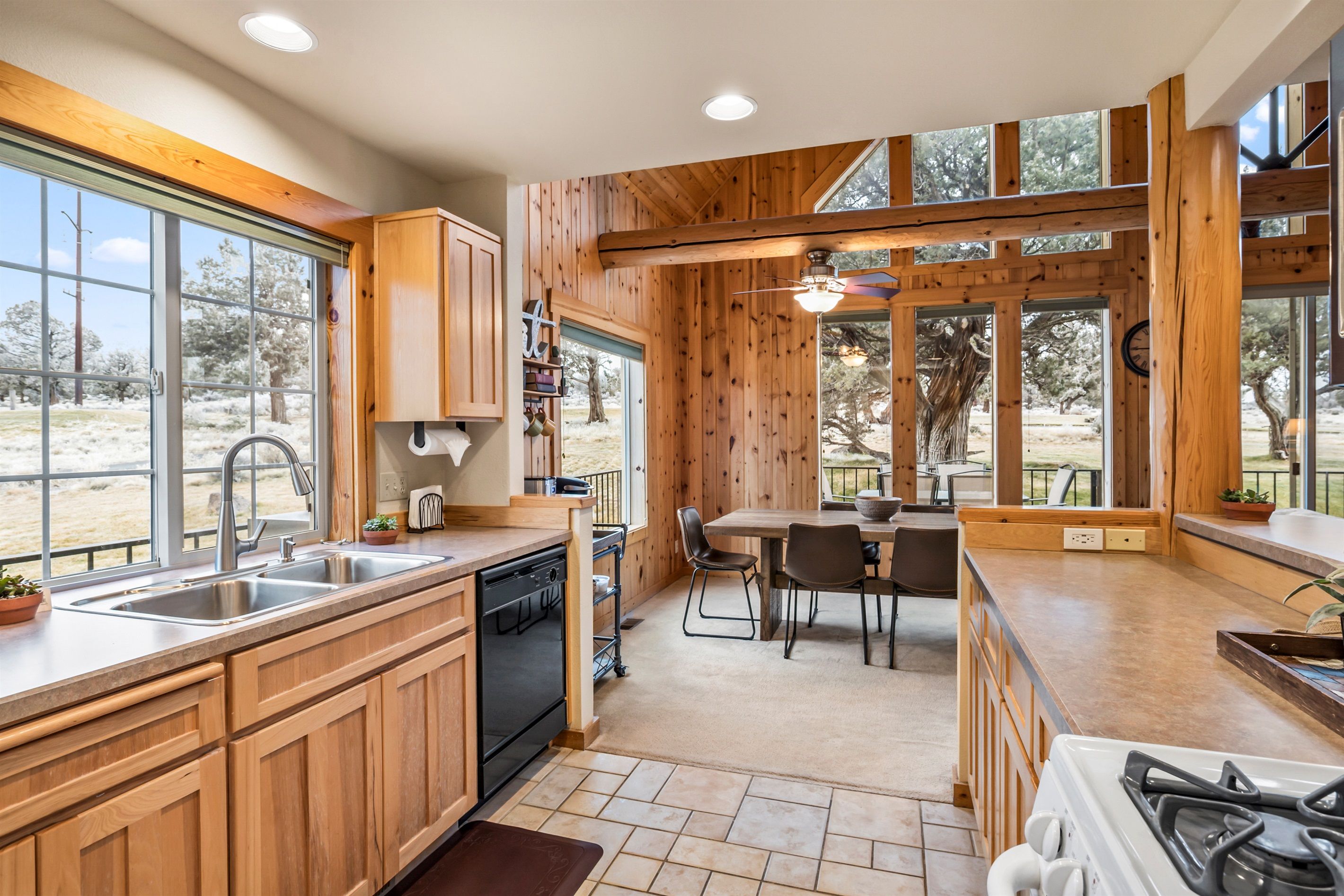A modern kitchen with wooden cabinetry, a dishwasher, a stove, and a dining area with a table and chairs.