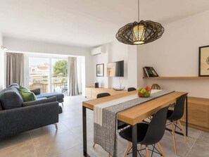 Ein modernes Wohnzimmer mit einer Couch, einem Esstisch, Stühlen, einem Fernseher und einem Balkon mit Vorhängen.