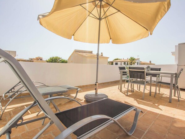 Eine Dachterrasse mit Tisch und Stühlen, einem großen Sonnenschirm und Blick auf umliegende Gebäude.