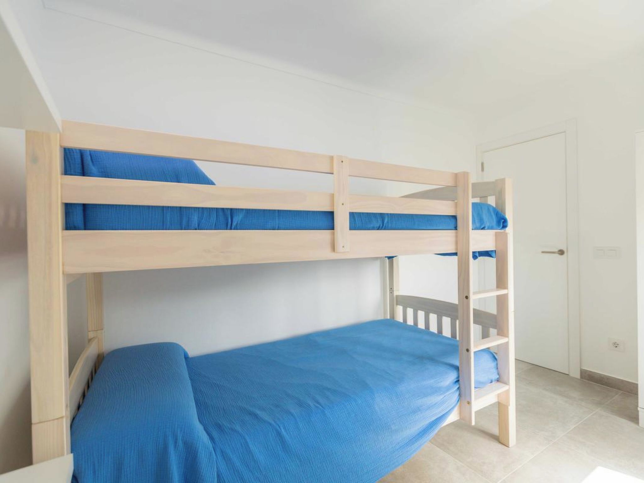 Ein Stockbett mit unterem Bett und einer Leiter, eine weiße Tür und ein gefliester Boden.