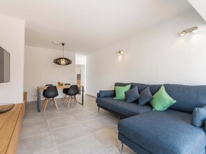 Ein modernes Wohnzimmer mit einer Couch, Sesseln, einem Esstisch und einem Fernseher.