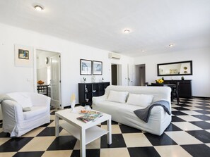 A living room with a checkered floor, white sofa, white armchair, and a coffee table with magazines. - Barcares II by Interhome (Alcúdia)