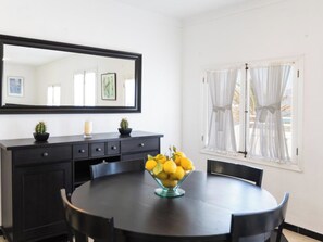 A dining area with a round table, chairs, a dark wooden cabinet, a mirror, and a window with sheer curtains. - Barcares II by Interhome (Alcúdia)