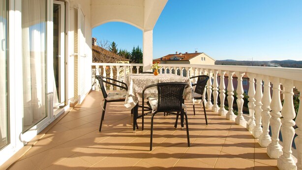 A balcony with a table and chairs, a white railing, and a view of buildings and trees. - Apartment 1978 by Interhome (Dracevac)