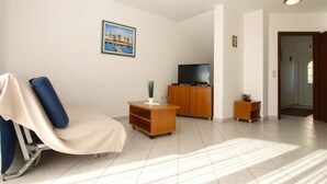A living room with a reclining chair, a television on a wooden cabinet, a small table with a plant, and a door leading to another room. - Apartment 1978 by Interhome (Dracevac)