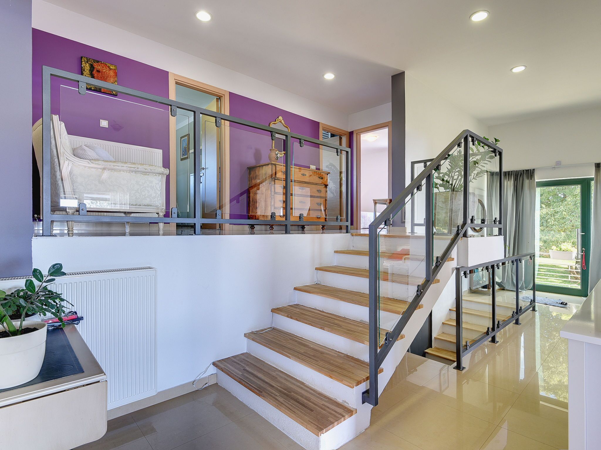 Una escalera con escalones de madera y barandales de metal que lleva a un rellano con un espejo y un aparador.