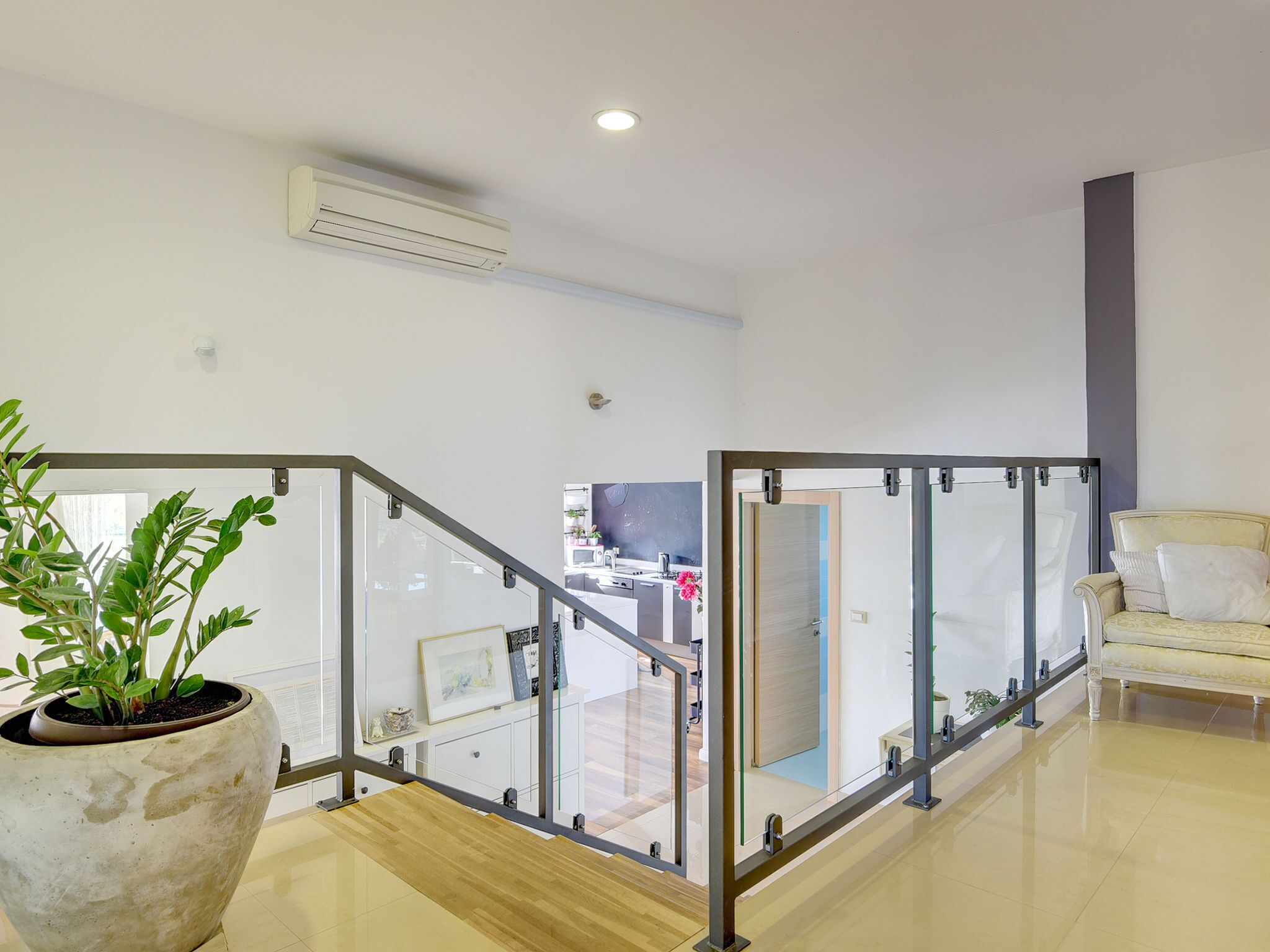 Un intérieur moderne avec un escalier à garde-corps en verre, une plante en pot et un canapé.