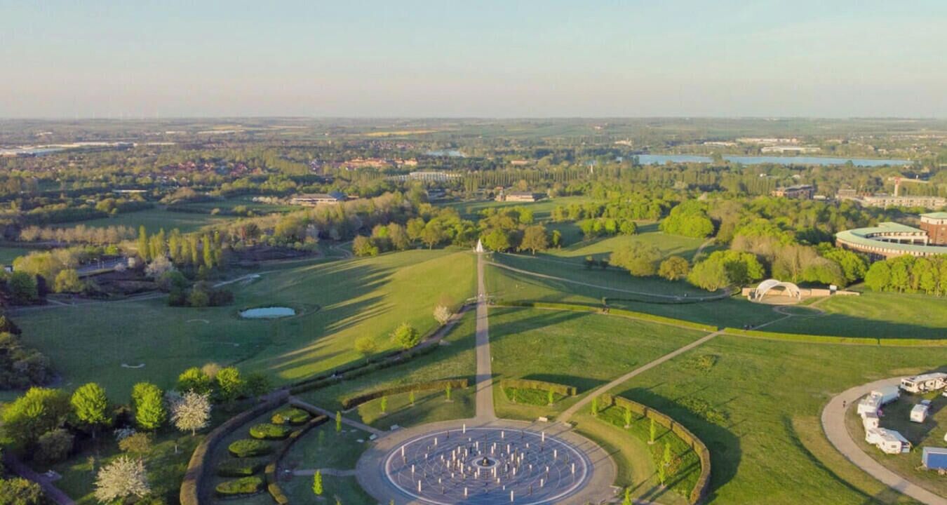 An aerial view of a park with a circular monument, pathways, and surrounding greenery.