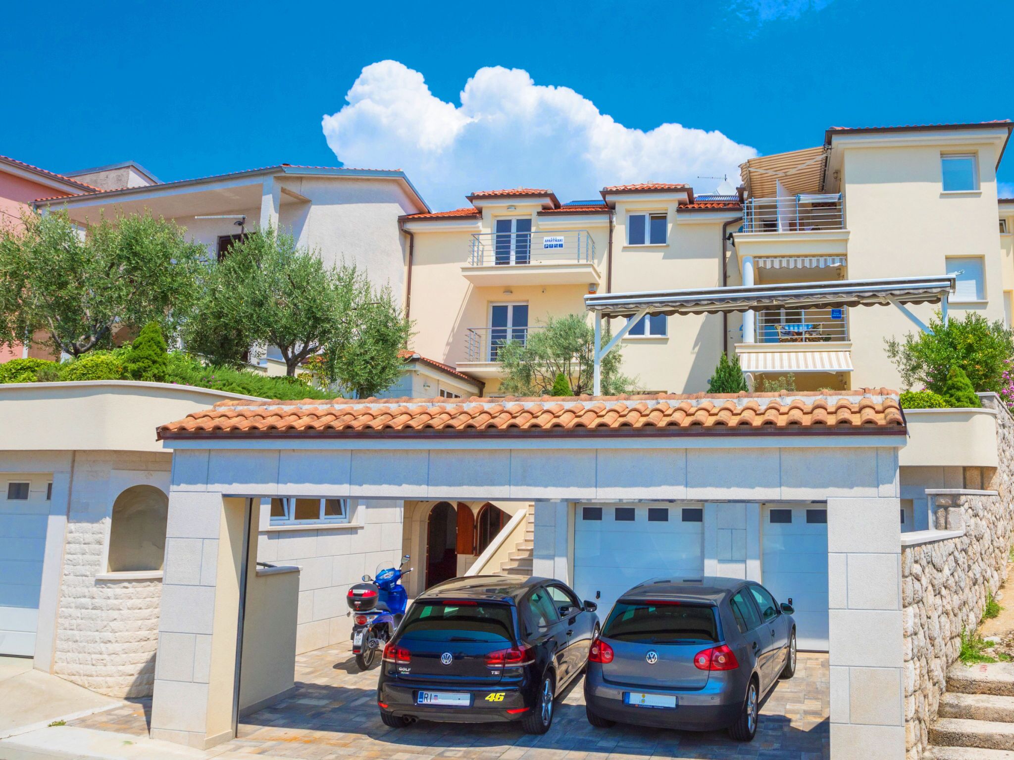 Ein Wohngebäude mit Garage, zwei geparkte Autos und blauem Himmel.