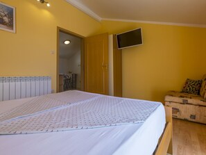 A bedroom with a bed, a television mounted on the wall, and a wooden chest of drawers. - BOZIDAR 1 zuti / HR-10438-01 by Interhome (Selce)