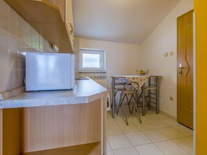 A compact kitchen with a refrigerator, a dining table with chairs, and a window. - BOZIDAR 1 zuti / HR-10438-01 by Interhome (Selce)