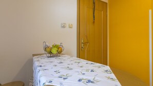 A room with a bed, a small table with a fruit basket, a chair, and a door. - BOZIDAR 1 zuti / HR-10438-01 by Interhome (Selce)