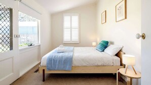 Een slaapkamer met een houten bed, een raam met zonwering, een nachtkastje met een lamp en twee ingelijste foto's aan de muur.