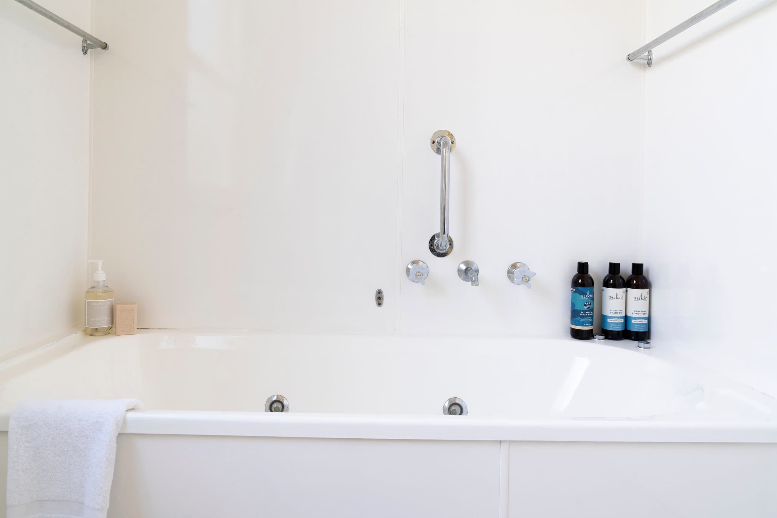 Una vasca da bagno bianca con un soffione manuale, due flaconi di shampoo e una saponetta.
