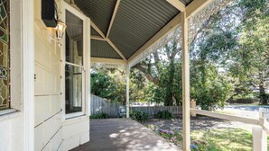 Een overdekte veranda met een houten terras, een witte omheining en een tuin met verschillende planten en bloemen.
