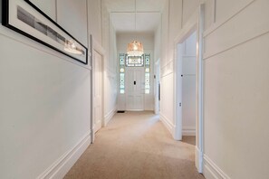 A hallway with a carpeted floor, white walls, and a framed picture on the left. There is a door at the end with a stained glass window above it. - Perfect Point Lonsdale Cottage (Point Lonsdale)
