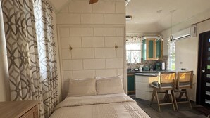 Une chambre avec un lit, une commode en bois, un ventilateur de plafond et une vue sur la cuisine.