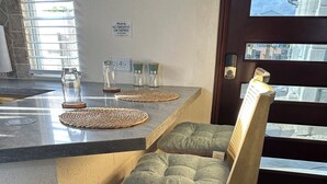 Un coin cuisine avec un comptoir-bar, un tabouret en bois avec un coussin et un panneau « interdiction de fumer » accroché au mur.