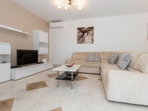 A modern living room with a flat-screen TV, a white sofa with patterned cushions, a coffee table, and a decorative wall piece. - House 2036 by Interhome (Rabac)