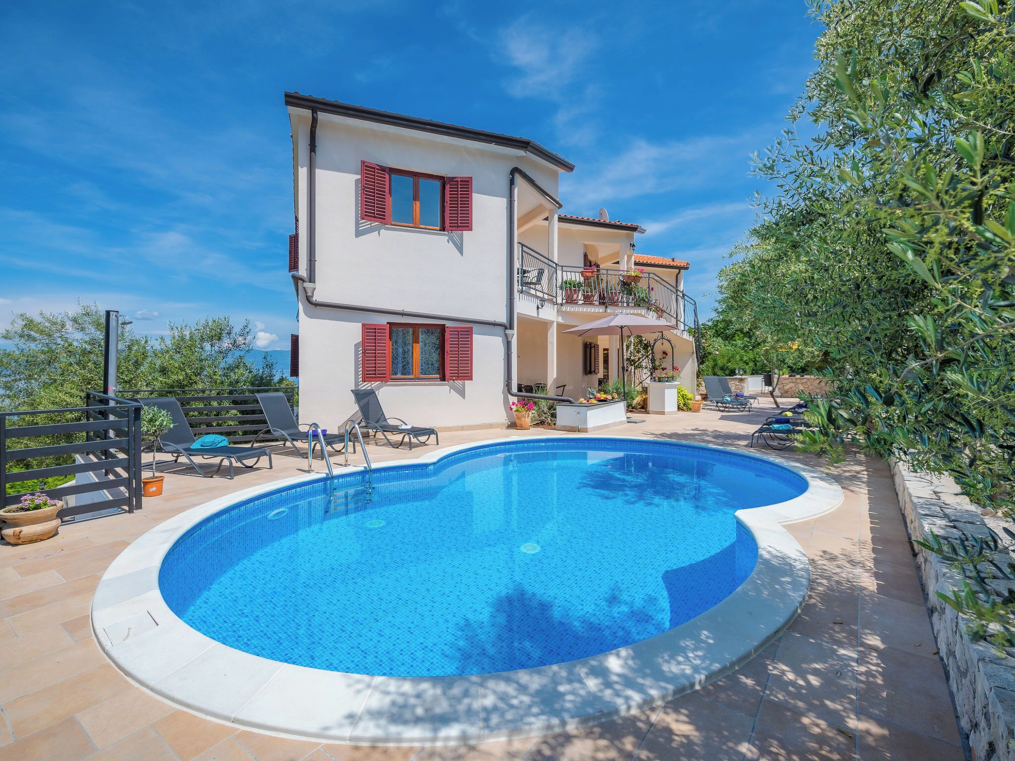 A two-story house with a swimming pool, outdoor furniture, and a garden.