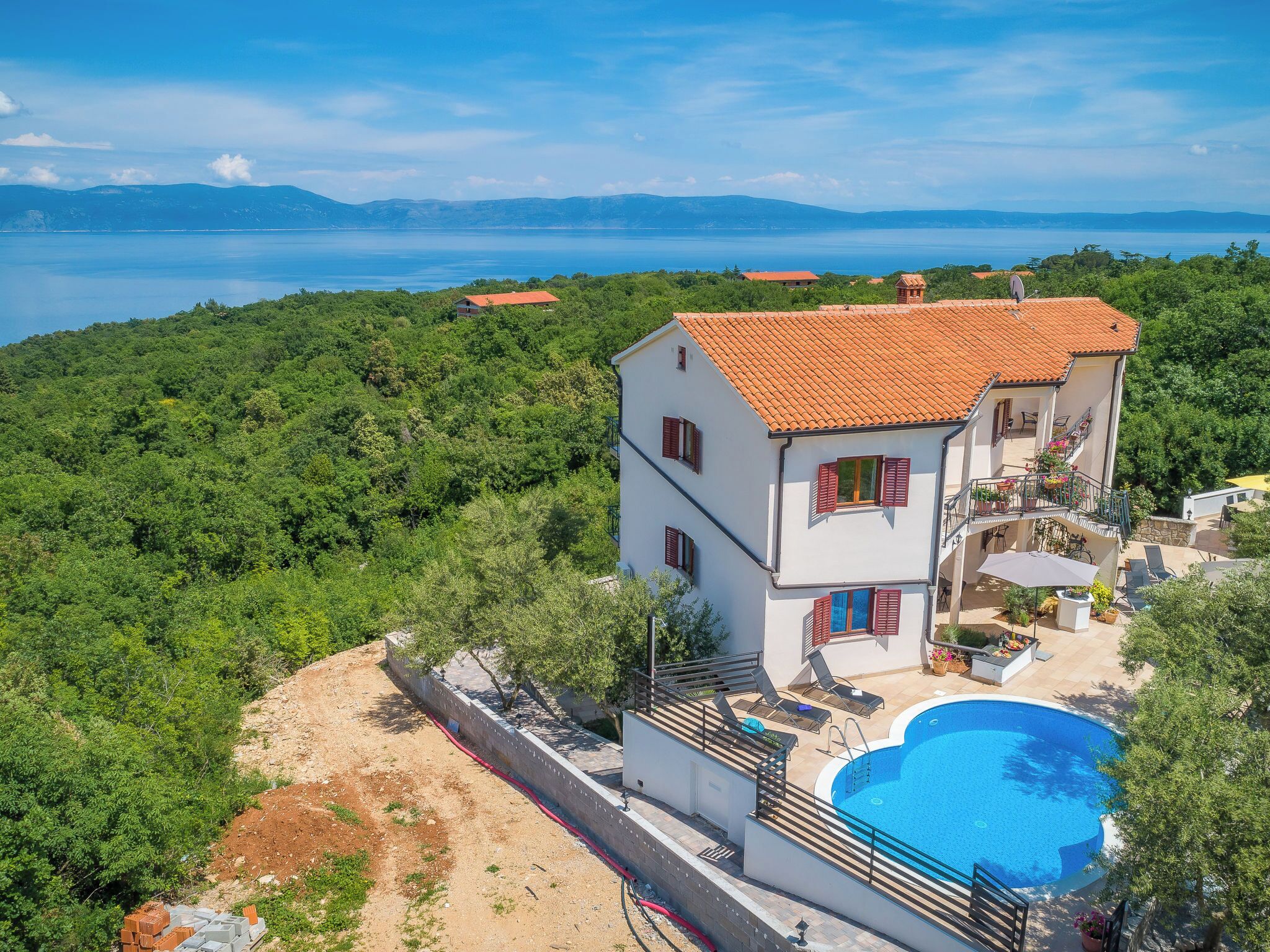 Casa de dos pisos con piscina, rodeada de vegetación y vista a un cuerpo de agua.