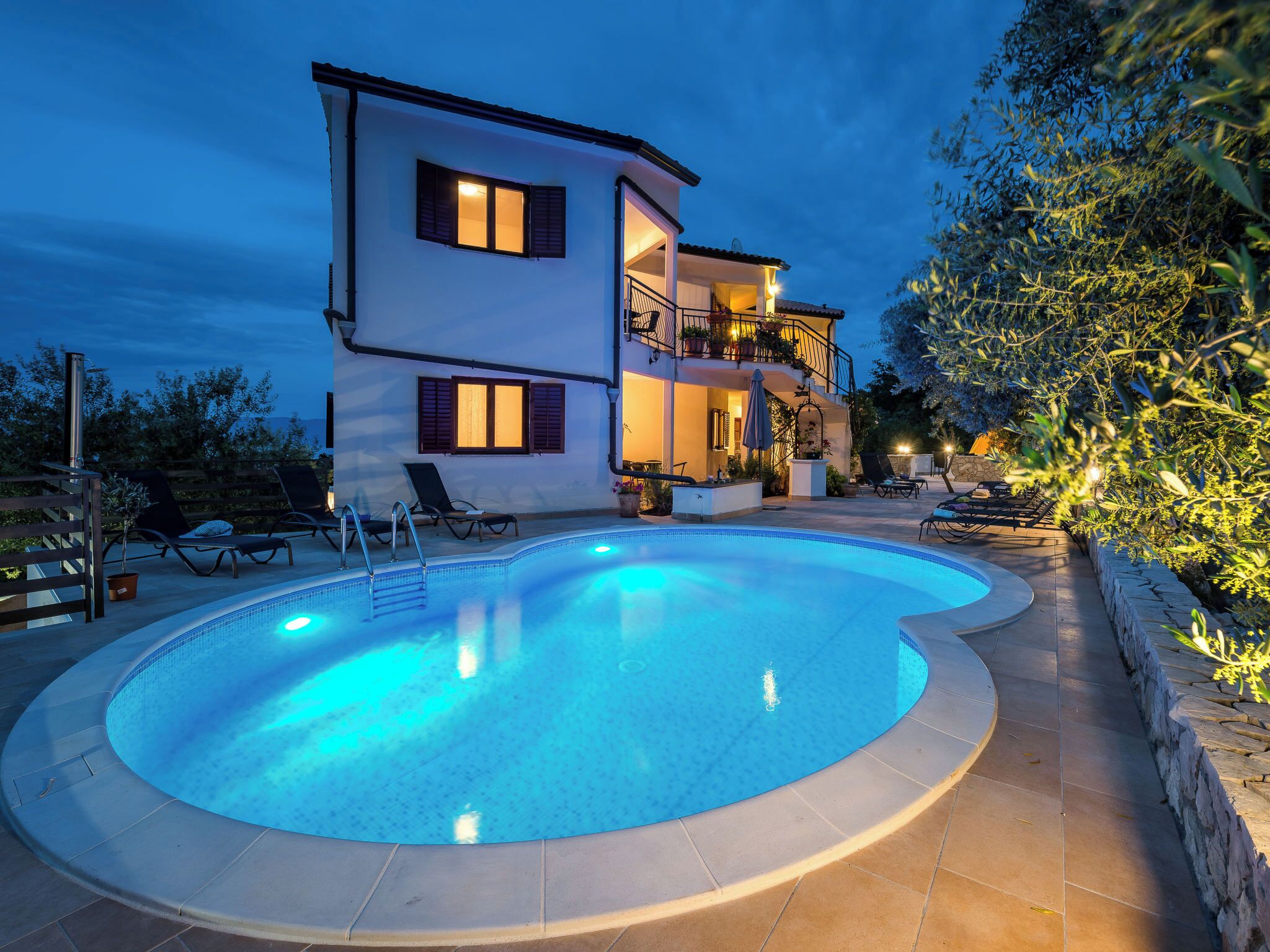 A two-story house with a swimming pool, outdoor furniture, and a balcony with plants.