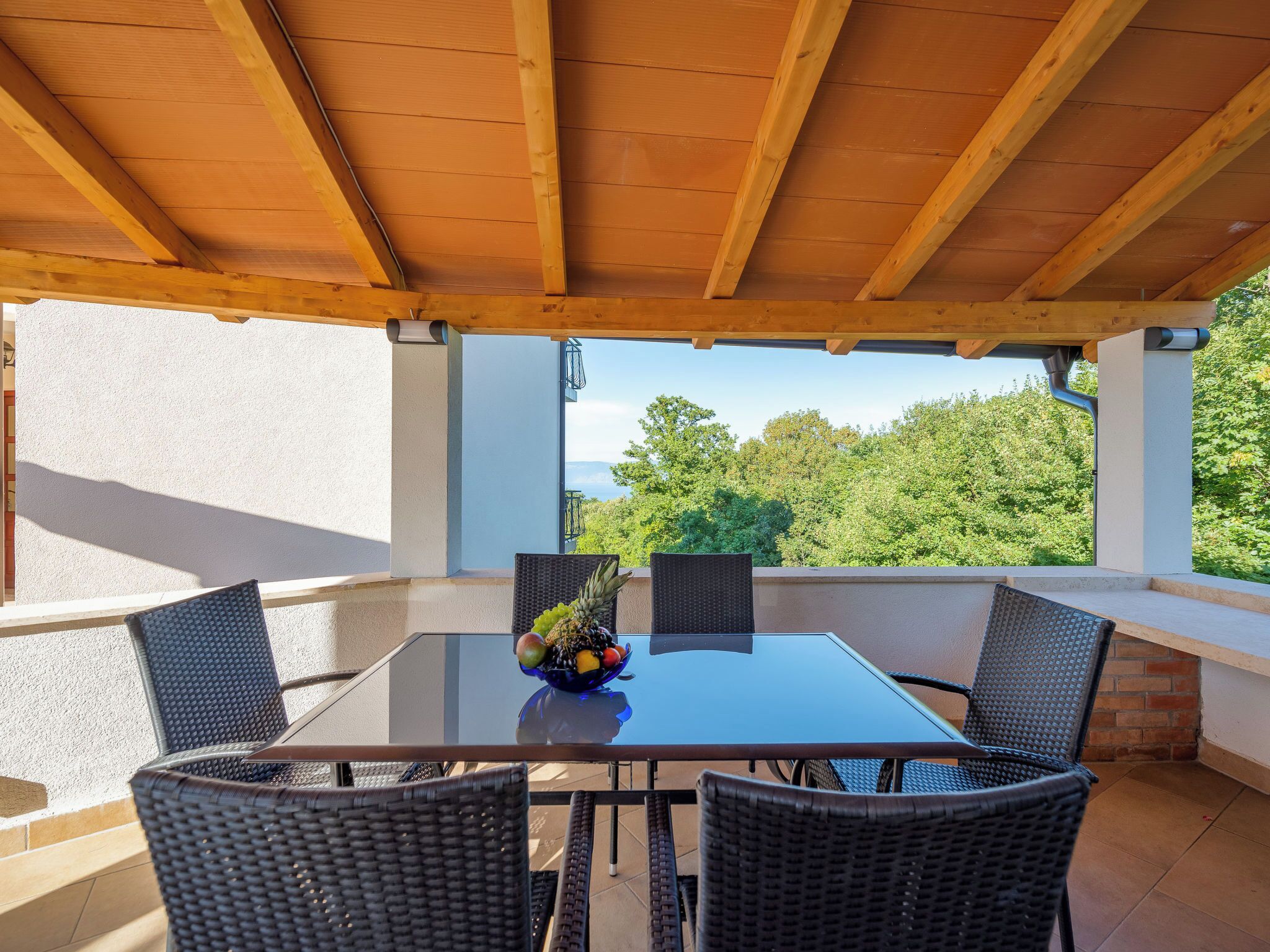 Una veranda esterna con tavolo e sedie, una ciotola di frutta e vista sul verde.
