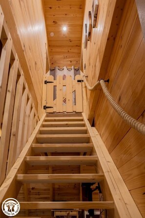 Eine Holztreppe mit Seilgeländer, die zu einem Raum mit Holzboden und -wänden führt.