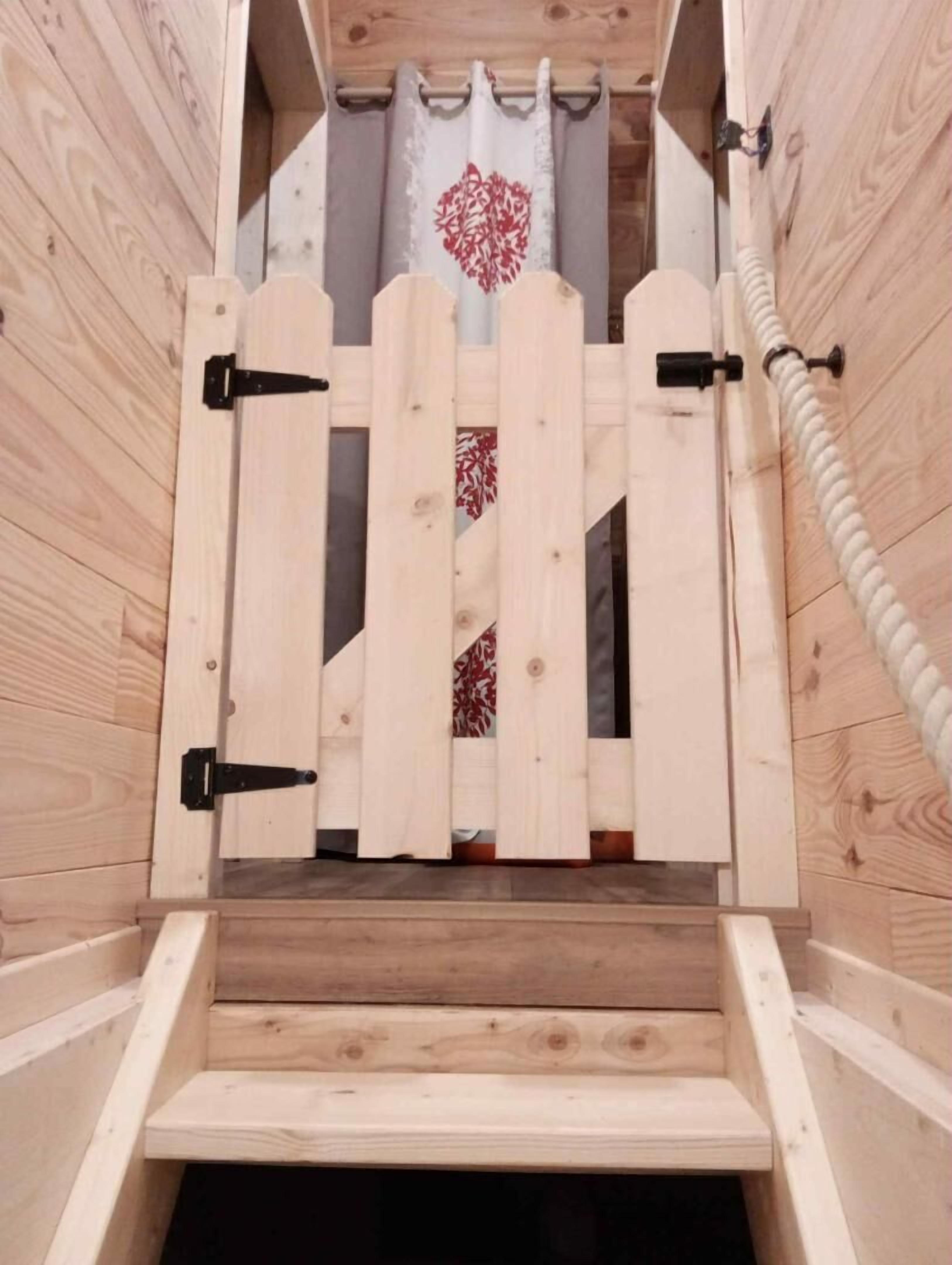 A wooden cabin with a simple entrance featuring a wooden gate and a rope handle.