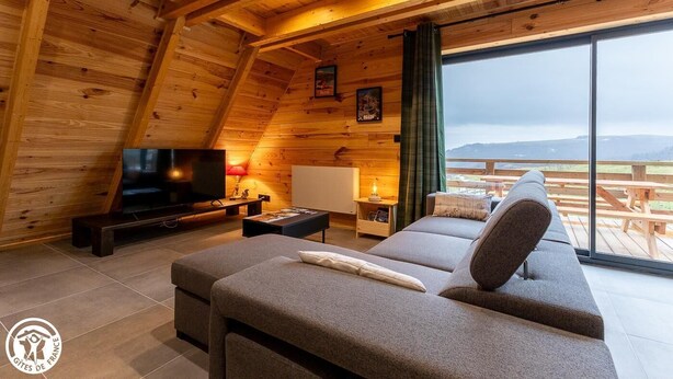 A cozy log cabin interior with a large TV, comfortable seating, and a scenic view. - Le Chalet du Pastoureau (BESSE ET SAINT ANASTAISE)