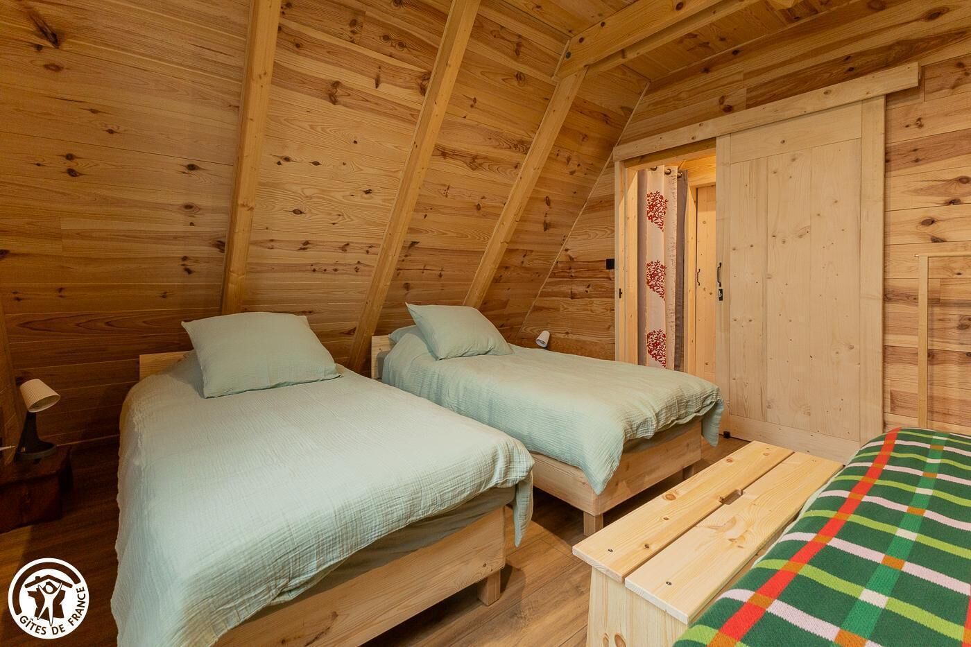 Une cabane en bois avec deux lits, un banc et une porte ornée d’un panneau décoratif.