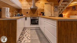 A modern kitchen with wooden beams, a built-in oven, and a coffee maker. - Le Chalet du Pastoureau (BESSE ET SAINT ANASTAISE)