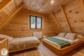 Ein gemütliches Schlafzimmer im Dachgeschoss mit holzgetäfeltem, geneigtem Giebeldach, einem großen Fenster, einem Bett mit bunter Decke und einem kleinen Nachttisch.