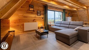 A cozy, wooden-floored living room with a large gray sectional sofa, a small coffee table, and a fireplace. - Le Chalet du Pastoureau (BESSE ET SAINT ANASTAISE)