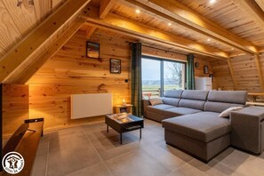 Ein gemütliches Wohnzimmer mit Holzboden, einem großen grauen Ecksofa, einem kleinen Couchtisch und einem Kamin.