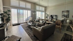 Ein geräumiges Wohnzimmer mit Sofa, Couchtisch und Sesseln. Ein Fernseher und eine Lampe stehen auf einem Beistelltisch.