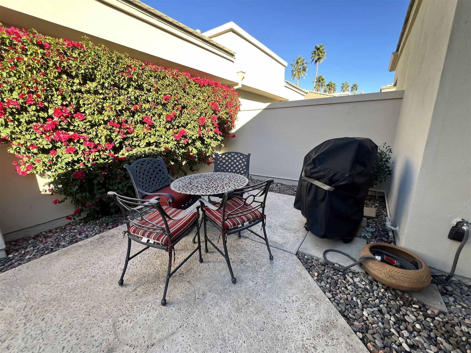 An outdoor patio with a round table and chairs, a barbecue grill, and a wall covered with flowering plants.