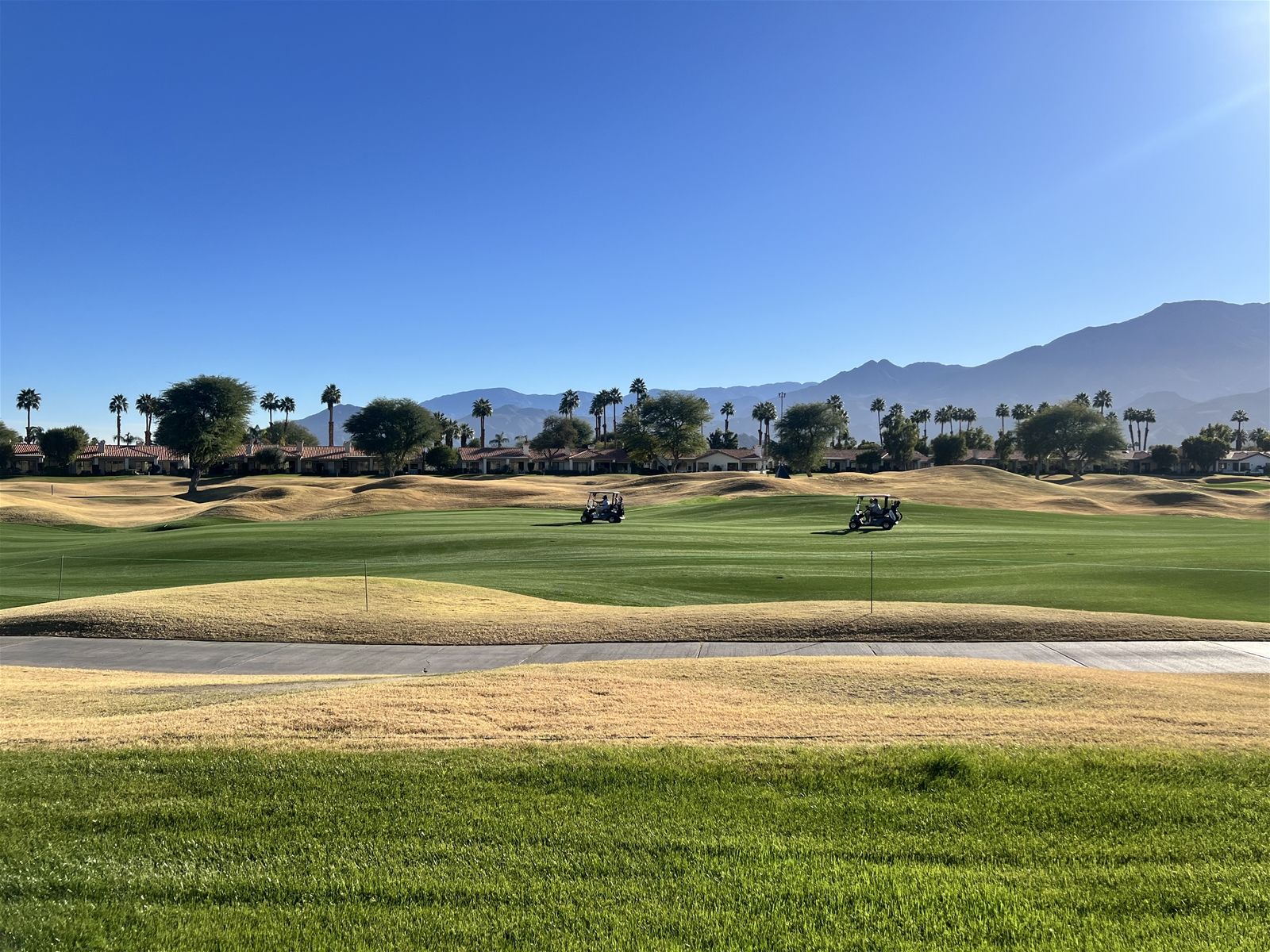 Ein Golfplatz mit Sandbunkern, blauem Himmel und Bergen in der Ferne.