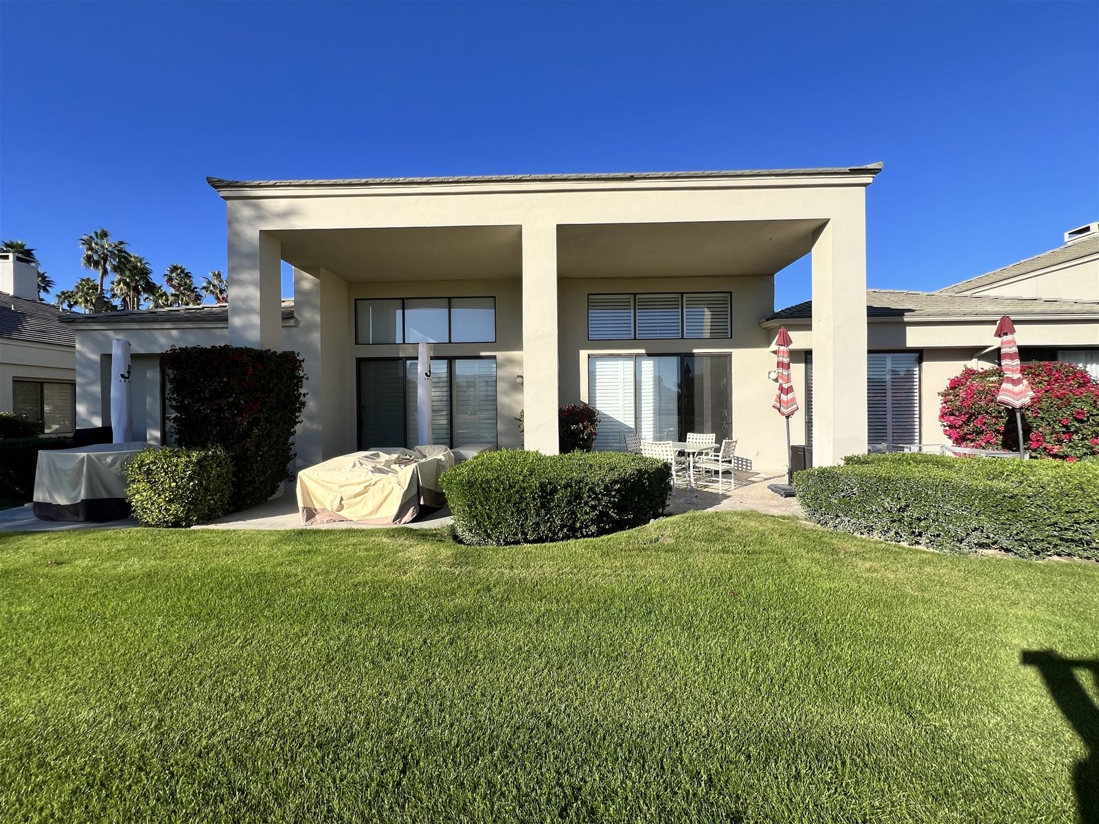A modern two-story house with a covered patio, a lawn, and a small garden area.