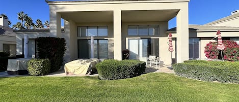 A modern two-story house with a covered patio, a lawn, and a small garden area.