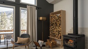 Ein gemütliches Zimmer mit Kamin, einem Sessel, einem Tisch und Blick ins Freie.