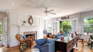 A spacious living room with a fireplace, wicker furniture, and a view of the outdoors. - Pau Hana - Spacious 4-bedroom house in quaint Nantucket with AC (Nantucket)
